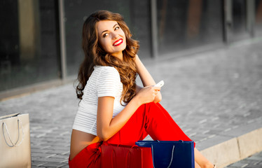 Young woman with shopping bags resting near shop