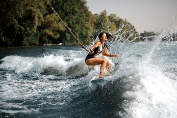 Smiling brunette girl riding on the wakeboard holding a rope - obrazy, fototapety, plakaty