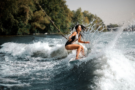Smiling brunette girl riding on the wakeboard holding a rope