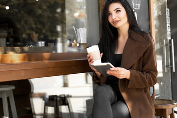 Beautiful girl uses a tablet and drinks coffee, sitting in a cozy cafe.
