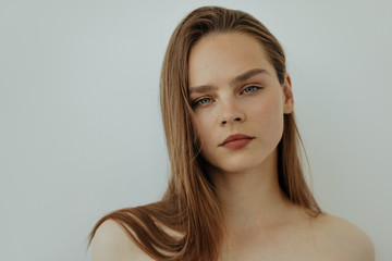 Portrait of attractive young girl with long hair and bare shoulders is looking at camera, isolated on white, copy spase