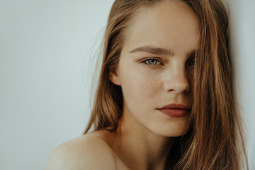 Natural beauty. Portrait of attractive young girl with bare shoulders is looking at camera, isolated on white, close up