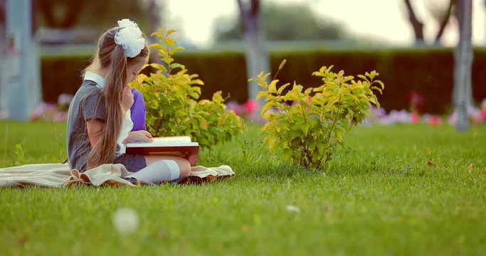 Young pretty school girl reading book in park
