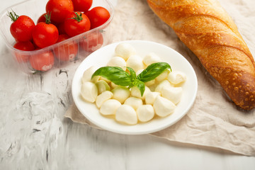 Mozzarella with basil leaves - fresh ingredients for Bruschetta, with cherry tomatoes and French baguette with copy space on a light background, top view