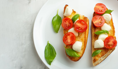 Bruschetta with tomatoes, mozzarella cheese and basil in a white plate. Traditional Italian snack or snack, antipasto. With space for writing