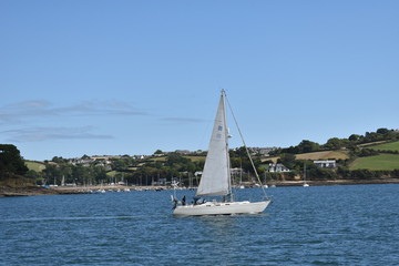 Sailboat sailing along the Cornish coast. Falmouth is one of the best locations in the UK to learn to sail, or improve your skills. Its sheltered deep harbor provides many sailing opportunities. 