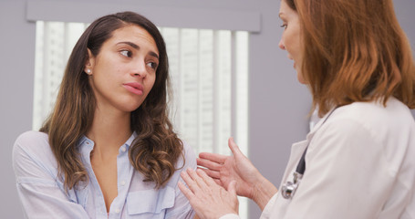 Close up of charming hispanic patient meeting with doctor about shoulder injury. Portrait of attractive latina discussing her arm trauma with mid aged medical doctor indoors office