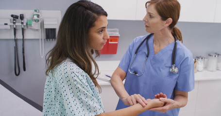 Fototapeta premium Medical nurse checking pulse of young patient indoors medical clinic. Close view of nurse using fingers to monitor patients vital pulse