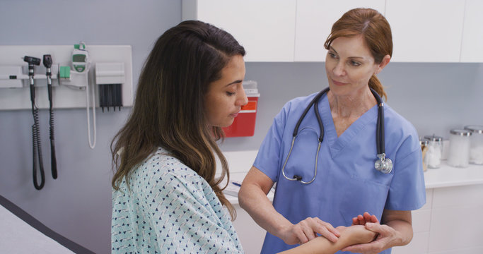 Senior medical nurse using two finger method to check blood rate of patient. Close up portrait of mid aged nurse checking young patients pulse indoors hospital clinic