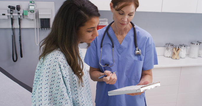 Close-up Portrait Of Medical Nurse Checking Medical History With Young Latina Patient. Portrait Of Hispanic Woman Going Over Health History With Senior Nurse