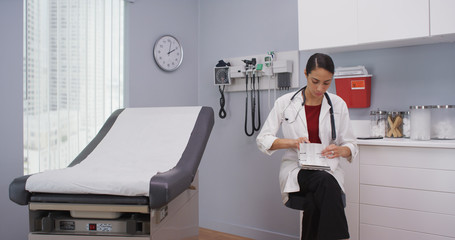 Close up of lovely latina doctor reviewing patients file indoors medical clinic. Attractive young doctor checking notes on clipboard for patients health history