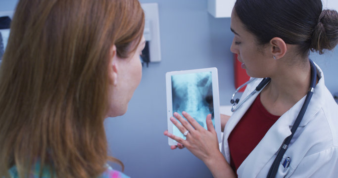 Young charming hispanic doctor using high tech tablet device to check pelvic bone xray. Close up of lovely latinca doctor holding portable tablet to review patients hip x ray