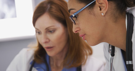 Tight shot of latina doctor discussing with elder medical colleague inside office. Close up of young hispanic medical doctor talking with senior colleague about patients health condition