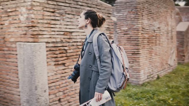 Camera follows young excited traveler woman with backpack expolring ancient historic red brick ruins of Ostia, Italy.