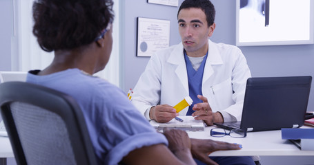 Portrait of young male doctor prescribing medication to senior female patient post surgery. Old African woman meeting with young latino doctor in office to receive prescription medication