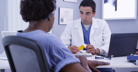 Portrait of young male doctor prescribing medication to senior female patient post surgery. Old African woman meeting with young latino doctor in office to receive prescription medication