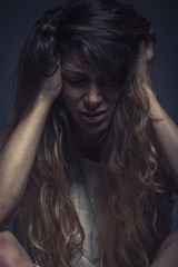 Depressed young woman sitting in a dark corner, crushed and alone