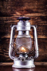 Old gas lantern burning on table and wooden plank background. Rust metal lamp with corrosion. Retro and vintage object concept