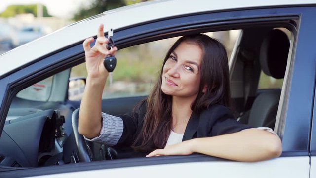 Portrait of a happy woman holding keys to new car and smiling at camera. Female driver in a car showing the car key. 4K UHD.