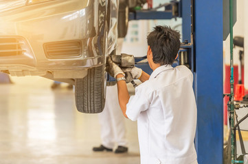 Car on lift to repair suspension in the garage with mechanic working underneath lifted car to change wheel hub and maintenance repair at service station  