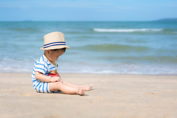 Fototapeta premium Portrait of a 10 months Asian baby boy with a hat sit in beach near sea in Phuket, Thailand. Summer, vacation, Travel and Holiday concept..