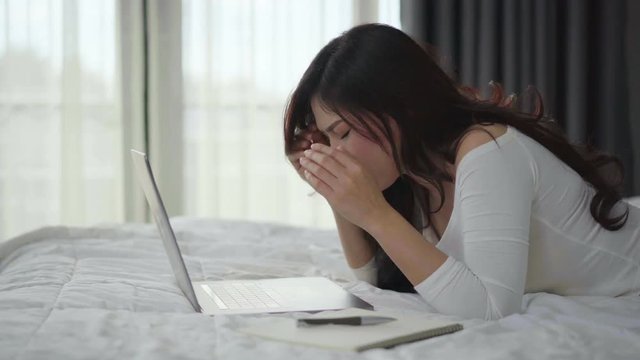 stressed woman using a laptop computer on bed