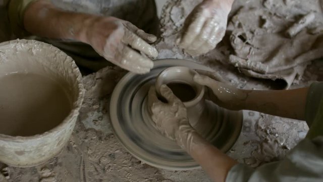 High angle shot with PAN of hands of unrecognizable female and male artisans throwing pot on spinning pottery wheel in workshop