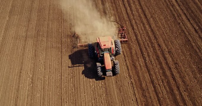 An aerial shot of a farmer in tractor cultivating arable land field just before seeding, sowing season.