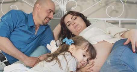 Young family is waiting for a newborn baby. A little daughter listens to the sounds of the newborn in the mother's belly.