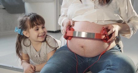 Pregnant woman with headphones on her belly. Future baby listens to music. - Powered by Adobe