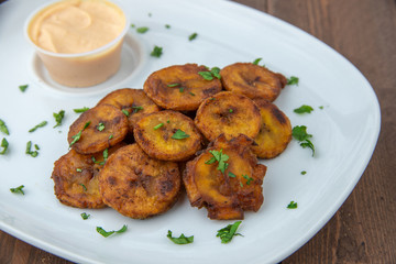 Fried plantains with aioli sauce served on white plate