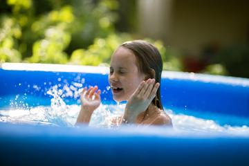 Smiling adorable seven years old girl playing and having fun in inflatable pool