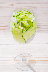 Refreshing water with slices of cucumber and basil leaves in a glass on a wooden table