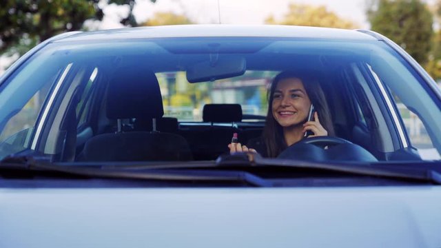 A young beautiful woman doing makeup in the car looking in the mirror and at the same time talking on the phone. 4K UHD video.
