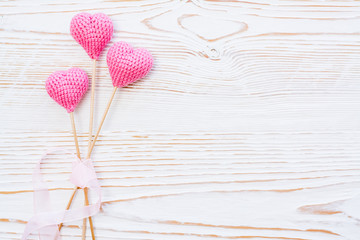 Obraz na płótnie Canvas Three pink knitted hearts on sticks tied with pink ribbon on a white wooden background