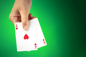 A hand holding two aces against a green background with a place for text