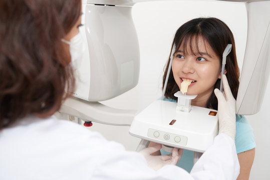 Asian teenage girl standing in digital cephalometric panorama x-ray machine