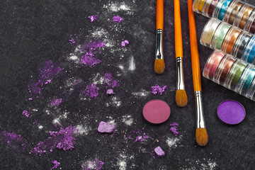 make up tools with pink and purple loose eye shadows lying on a black background. concept of...