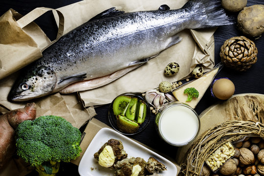 Products containing phosphorus salmon fish, pine nuts, peanuts, anchovy, cheese, milk, eggs, broccoli, kiwi, potatoes, meat, beans garlic on a round cutting board and black wooden background