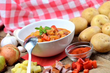 Potato and sausage goulash, pepper, onion, spoon and garlic on wooden table