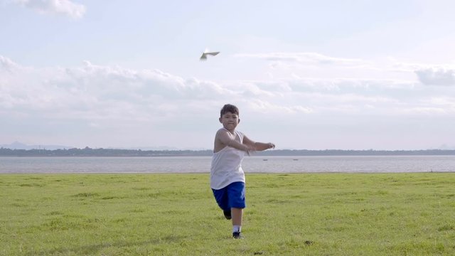 Little boy old 7 years Happy with a running and throwing paper airplane on meadow in summer in nature Sunset time. 4K Video Slow motion