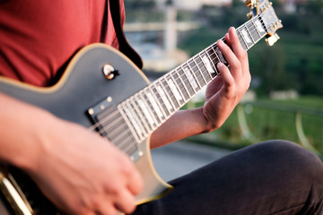 hands of guitarist playing electric guitar outdoors, evening