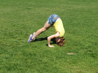 Teenage redhead girl in denim shorts performs a headstand. Yoga outdoors, fitness training,...