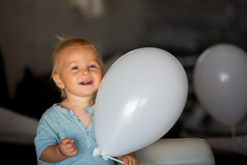 Little baby boy, celebrating his first birthday, having cake and balloons