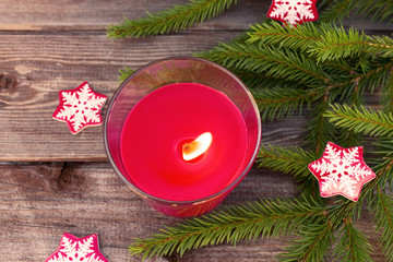 Christmas decorations, fir branches and red flaming candle on vintage wooden board background