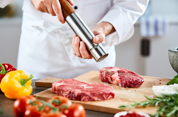 Chef grinding peppercorns over a raw steak