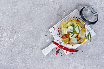 Top view of marinated feta cheese with olive oil and spice of red chili pepper and rosemary in glass jar on white wooden board
