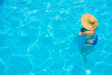 Woman in a pool with hat relaxed and rested.