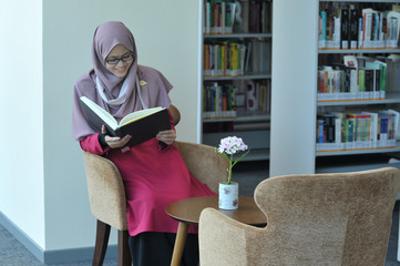 A young beautiful muslimah student studying in a library.