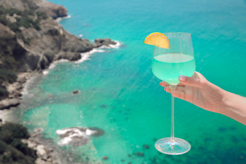 Summer Cheers! Cropped image of Hand with blue curacao cocktail glass over turquoise lagoon exotic bay. Lifestyle summertime vacation concept. Black sea coast, Crimea.